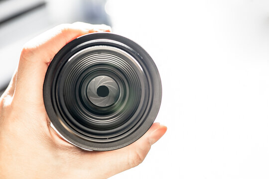 Person’s hand holding black digital camera lens, look insight shutter with sunlight background. Closeup photography equipment, front view. Concept of photographer, professional item with copy space.