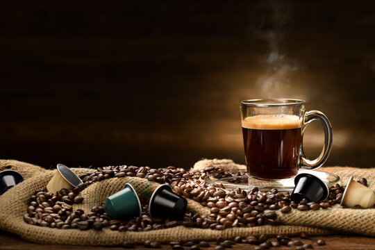 Cup glass of coffee with smoke and coffee beans and coffee capsules on burlap sack on old wooden background