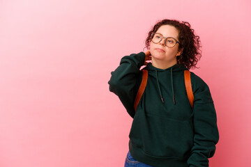 Young student woman with Down syndrome isolated on pink background touching back of head, thinking...