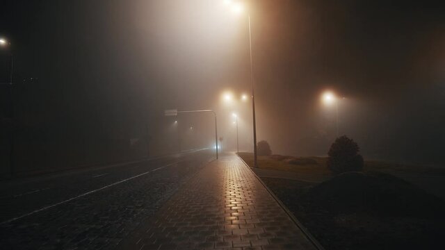 Slowmotion night view of cinematic mystical empty street with no people. Misterious horror scene. Darkness, thick fog, rainy weather.