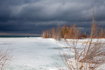 A winter storm approaches the shores of Southern Georgian Bay in Lighthouse Point, Collingwood. Ice extends across the bay with gloomy, menacing clouds approaching