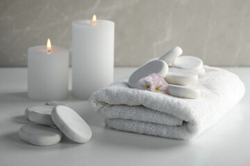 Spa stones, towel and burning candles on white table