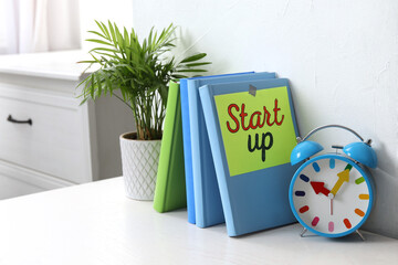 Book with words Start Up, plant and alarm clock on white wooden table indoors