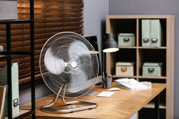 Modern electric fan on table in office - obrazy, fototapety, plakaty