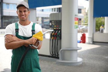 Worker with fuel pump nozzle at modern gas station