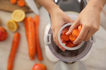 Young woman putting fresh slices of carrot into juicer at table, top view