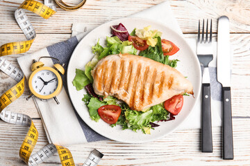 Plate of appetizing food, alarm clock and measuring tape on white wooden table, flat lay. Nutrition regime