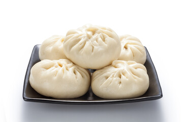 Fototapeta na wymiar Fresh baozi (Chinese steamed buns) in a black ceramics plate. Isolated on white background.