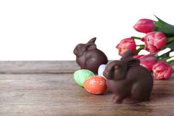 Chocolate Easter bunny, eggs and tulips on wooden table against white background. Space for text