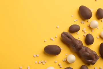 Flat lay composition with chocolate Easter bunny, eggs and candies on yellow background. Space for text