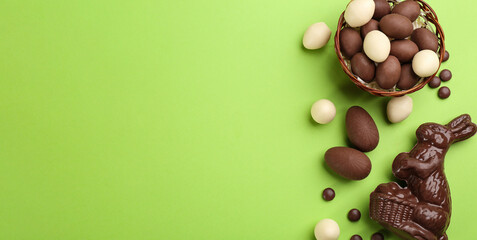 Flat lay composition with chocolate Easter bunny, eggs and candies on green background. Space for text