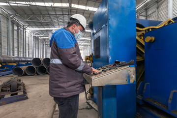 The operator is working with protective face mask on the control panel in the spiral welded pipe factory.