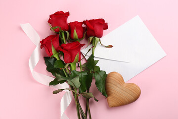 Flat lay composition with beautiful red roses and envelope on pink background. Valentine's Day celebration