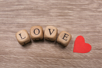 Mini cubes with letters forming word Love near red paper heart on wooden background, flat lay