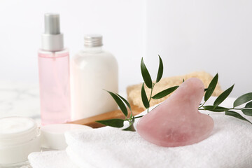 Obraz na płótnie Canvas Rose quartz gua sha tool, cosmetic products and towel on table