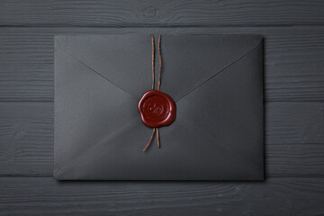 Envelope with wax seal on black wooden background, top view