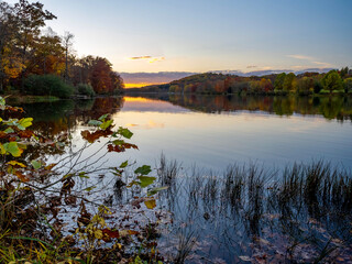 Keystone Lake in Keystone State Park in West Moreland County in the Laurel Highlands of Pennsylvania in the fall right before sunset with the fall foliage and trees reflecting in the water.