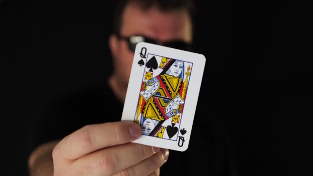 Mysterious anonymous card player with sunglasses and pocker face presents queen of spades