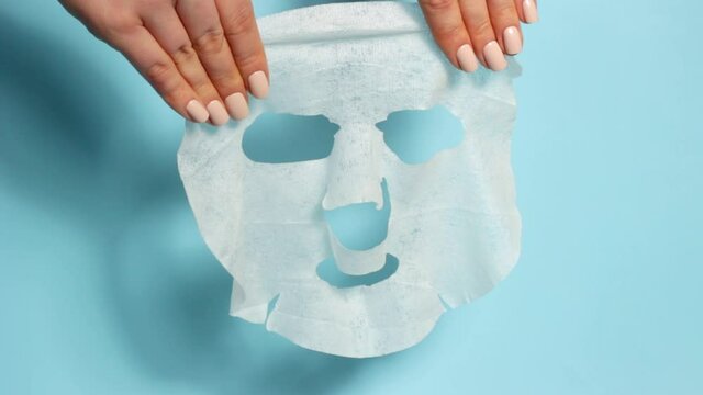 Female hands hold sheet of facial mask on a blue background front view.