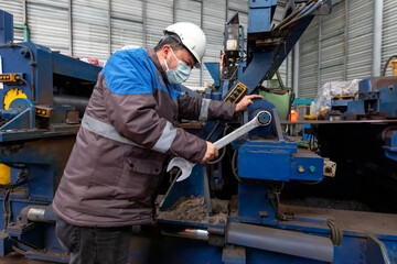 Worker is repairing to machine with screw wrench. A wrench or spanner is a tool used to provide grip and mechanical advantage in applying torque to turn objects usually rotary fasteners, such as nuts.