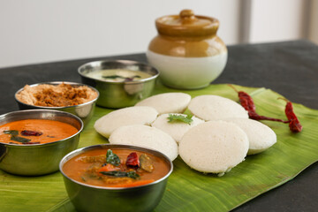 Many Idli idly sambar coconut chutney , tomato chutney serving breakfast vegetarian food South Indian restaurant on banana leaf Kerala Tamil Nadu India Sri Lanka. healthy steamed rice cakes .