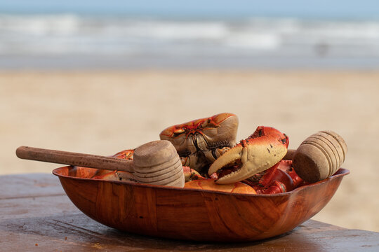cooked crab served in a rustic bowl with wooden hammers on a wooden table on a beach in front of the sea. Typical snack from the northeastern Brazilian beaches