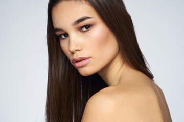Fototapeta premium Pretty brunette naked shoulders long hair close-up light background