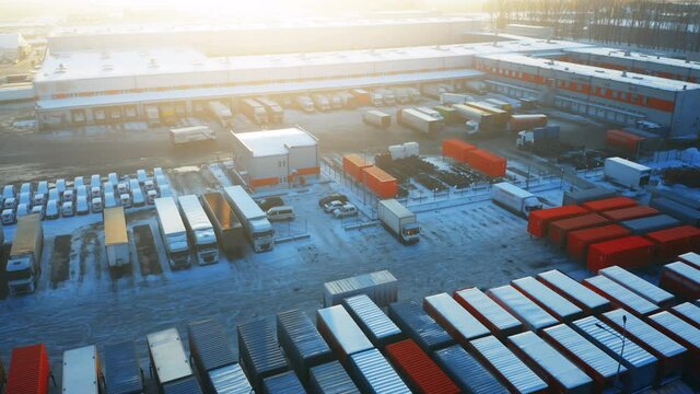 Logistics park with loading hub and many cargo (freight) containers on a parking lot. Semi-trailers trucks stand at warehouse ramps and wait for load and unload goods. Aerial view