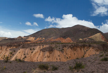 Fototapeta premium High in the cordillera. Panorama view of the orange rocky cliffs, precipice and colorful mountains under a blue sky.