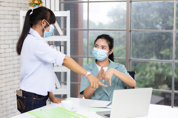 Two Asian women are discussing working using sign language and wearing masks to prevent the spread of the Covid-19 virus.