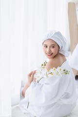 Obraz na płótnie Canvas Asian woman in spa clothing in bedroom with white curtains. A beautiful Asian young woman smiling in a white bathrobe.