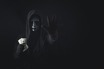Dangerous anonymous hacker man in hooded showing stop gesture and holding banknote, break security data and hack password with personal Bank account. Internet crime cyber attack security concept
