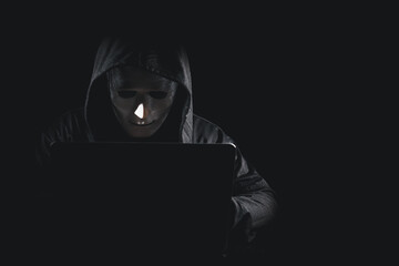 Dangerous anonymous hacker man in black hooded, white mask use computer and mobile phone, break security data corporate server. He working on black background. Internet crime, cyber attack security.