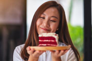 A beautiful young asian woman, waitress or a chef holding and serving a piece of red velvet cake in wooden tray