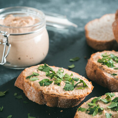 Close up view of slice bread with homemade turkey pate and fresh green parsley on black slate board over gray concrete background, Copy space. Shallow DOF