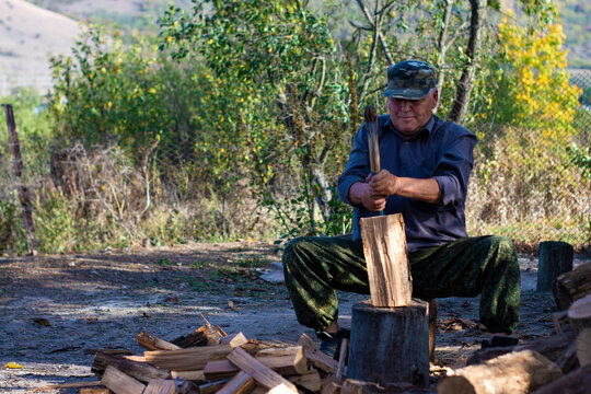 Old Man Chop Wood Sitting. View From The Front. Outdoors In The Daytime.