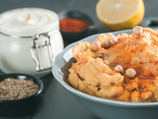 Homemade hummus with olive oil in gray bowl and ingredients. Traditional middle eastern appetizer hummus on gray background - healthy vegan paste snack. Vegetarian diet,nutrition protein food concept