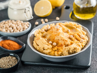 Homemade hummus with olive oil in gray bowl and ingredients. Traditional middle eastern appetizer hummus on gray background - healthy vegan paste snack. Vegetarian diet,nutrition protein food concept