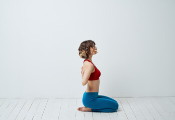 Obraz premium A woman in blue leggings sits on a light floor indoors and holds her hands behind her back