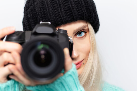 Close-up portrait of young girl taking photo on DSLR camera against white background.