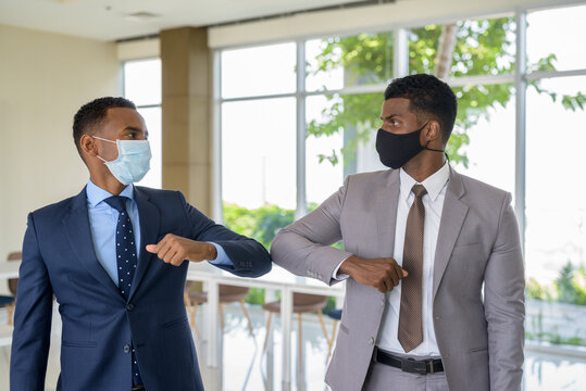 Two African Businessman Wearing Medical Mask While Greeting With Elbow Bump Greeting At Office. Social Distance Concept During The Coronavirus Epidemic.