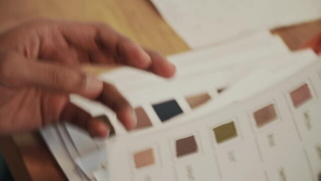 Close-up of hands browsing through colored fabric swatches for Dress design choices. Handheld Camera style.