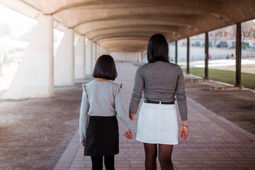 Rear view young mother and daughter walking together on a park.
