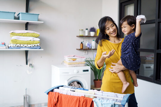 asian mother a housewife drying and hanging clothes in loundry room at home while carrying her baby