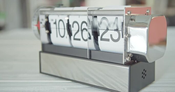 Flip clock or flap clock on white table. An electromechanical, digital time keeping device with time indicated by numbers sequentially revealed by a split-flap display, operates only in one direction.
