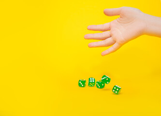A lot of green dice fall from the hand on a yellow background with space for text: board games, selective focus on the hand, a photo in motion