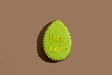 Happy easter bakery. Handmade gingerbread. Festive decoration. Sweet cookie egg with green icing and holiday wish text isolated on beige copy space.