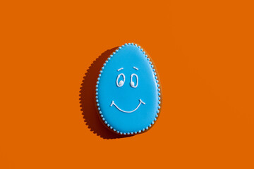 Happy easter bakery. Traditional gingerbread. Festive decoration. Pretty cookie figure egg with blue icing and white painted smiling face isolated on orange copy space.