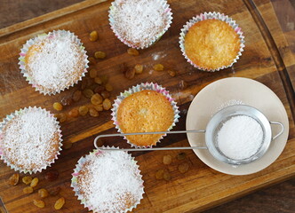 Small homemade muffins with powdered sugar baked in paper tins on an ancient wooden background.