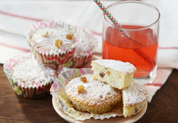 Small homemade cakes with powdered sugar, baked in paper tins with a glass of juice.